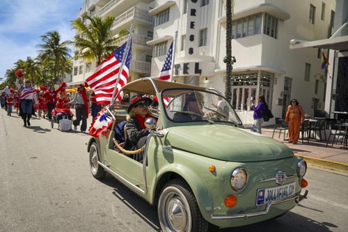 people driving vintage Fiat with American flags on the back
