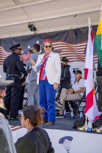 people on stage, woman in front is smiling and holding American flag